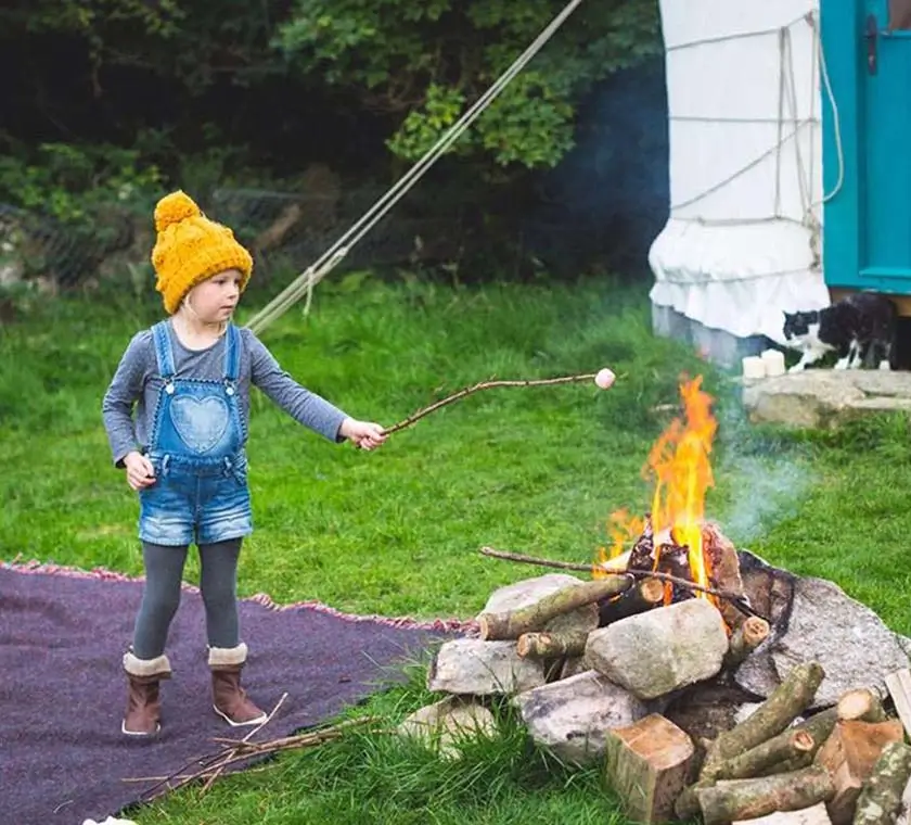 A young girl glamper trying to roast her mashmallow on top of campfire with a stick.